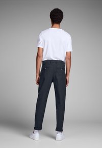 Mörka byxor med rutmönster och uppvikta fållar, två bakfickor, kombinerade med en enkel vit t-shirt och vita sneakers, sedd bakifrån.