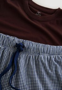 Bordeaux tričko s kulatým výstřihem v kombinaci s elastickými kalhotami vzorovanými modro-bílým houndstooth, které mají stahovací tmavě modrou šňůrku.