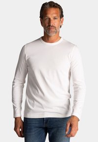 Wit katoen shirt met lange mouwen en ronde hals, met een subtiele logo op de borst, gecombineerd met blauwe denim jeans.