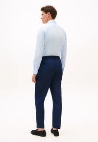 Ανοιχτό μπλε πουκάμισο με κουμπιά, σκούρο μπλε παντελόνι και μαύρα παπούτσια χωρίς κορδόνια. Διαθέτει μακριά μανίκια, μανσέτες και λεία υφή.