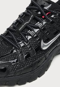Μαύρο αθλητικό παπούτσι Nike με υφές από δίχτυ και γυαλιστερό δέρμα, αντανακλαστικό ασημί λογότυπο Swoosh, λεπτομερής κορδόνια και ετικέτα «III BOOT-TRAIN SERIES» στα κορδόνια.