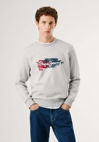 Sudadera gris con cuello redondo, que presenta un colorido logo de "Pepe Jeans" en la parte frontal. Combinada con jeans azul oscuro, mostrando un diseño casual.