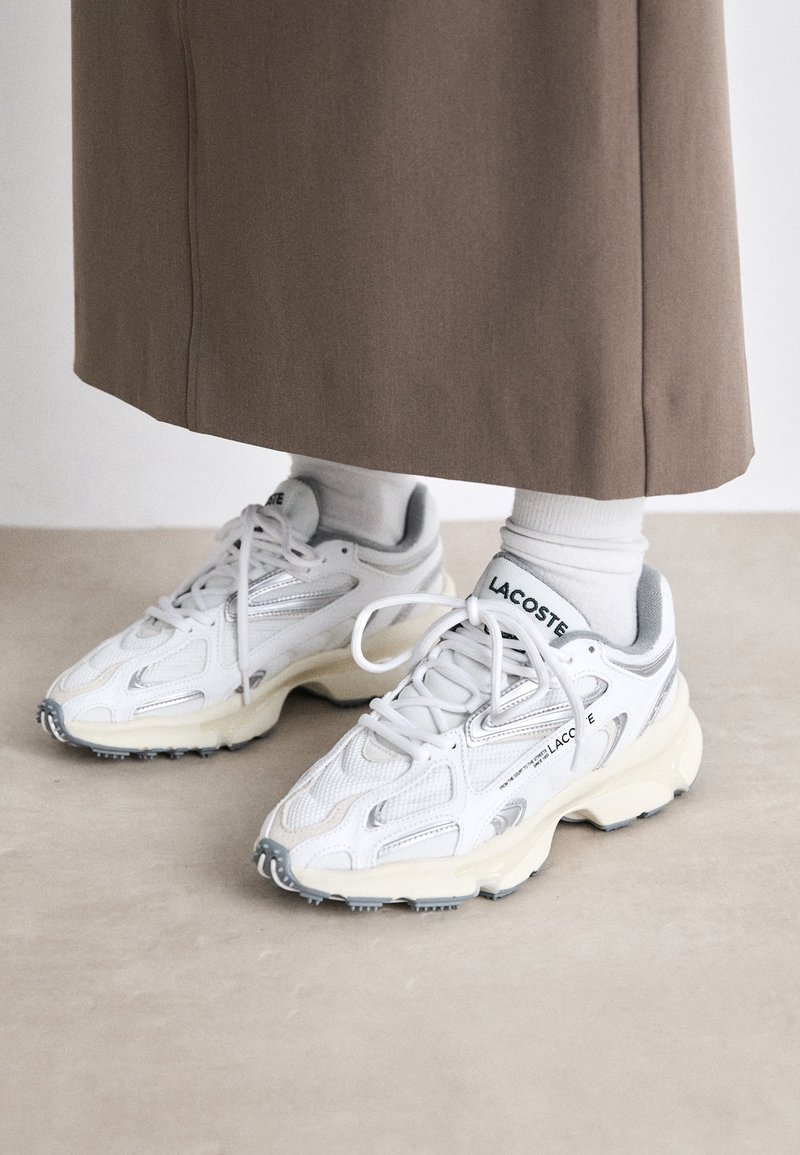 Vita sneakers med mesh- och läderpaneler, med en texturerad sula och silverdetaljer. Logotyp synlig på sidan och tungan.