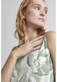 Top sin mangas de tela suave con estampado floral en verde claro, que presenta un corte holgado, un brillo sutil y tirantes delgados.
