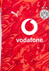 Rød mønstret sportstrøje fremstillet af åndbart stof, med hvid Puma-logo, Vodafone-logo og Borussia Dortmund badge.