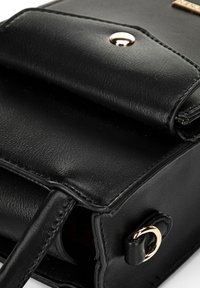 Sac à main en cuir noir avec un design structuré, fermeture à rabat arrondi, accents en métal doré et surface lisse et texturée.