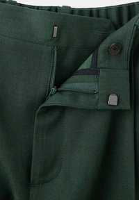Pantalon en tissu vert foncé avec une fermeture éclair ouverte, un crochet en métal et un bouton à la taille.