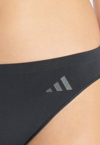 Svarta bikiniunderdelar med en slät yta, som har ett brettband och en subtil logodetalj i en ljusare nyans på sidan.