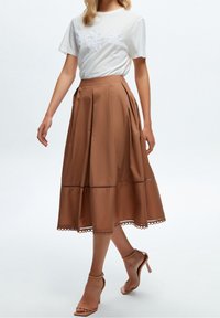 T-shirt blanc avec broderie florale associé à une jupe midi plissée marron avec un ourlet en forme de vagues et des sandales à talons.