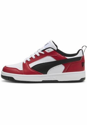 Niski sneaker z panelami ze skóry w kolorach czerwonym, białym i czarnym, białymi sznurowadłami, czarnym paskiem z logo i grubą białą podeszwą z czarnym spodem.