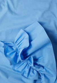 Tissu bleu clair avec un design à volants, présentant des coutures froncées le long des bords, une texture douce et une finition lisse.