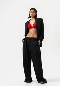 Rode kant bralette en high-waisted zwarte wijde broek, gelaagd met een oversized zwarte blazer. Getextureerde stoffen met strakke lijnen.