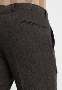 Donkergrijze, gestructureerde stoffen broek met een getailleerde pasvorm, voorzien van een achterzak en subtiele stikdetails. Tailleband in een lichtere tint.