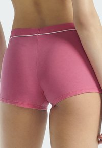 Shorts en coton rose avec une texture lisse, présentant une ligne d'accent blanche au niveau de la taille et une coupe ajustée.