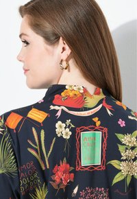 Blusa con motivo floreale caratterizzata da uno sfondo scuro, colori vivaci e un collo a V. Orecchini a cerchio dorati completano il look.