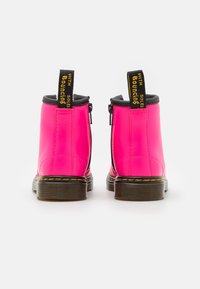 Botines de cuero rosa intenso con detalles en negro, que cuentan con cremallera lateral y etiquetas de marca amarillas en las lengüetas. Suelas de goma texturizadas.