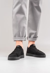 Czarne dziane sneakersy z sznurowaną konstrukcją, z teksturowaną cholewką i grubą gumową podeszwą. W zestawie z szarymi spodniami z mankietami.