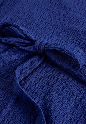 Tumesinine tekstuuriga kangas, millel on samast materjalist ja värvist seotud lips, rõhutades kanga detaili ja sõlme kuju.