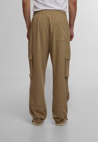Beige cargo bukser med elastisk talje, sidelommer og syningsdetaljer. Det lette stof giver en afslappet pasform.