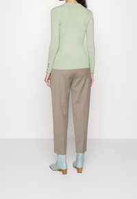 Jasnozielony dopasowany sweter z długimi rękawami i ozdobnymi guzikami, zestawiony z beżowymi, dopasowanymi spodniami oraz bladoniebieskimi botkami na prostym tle.