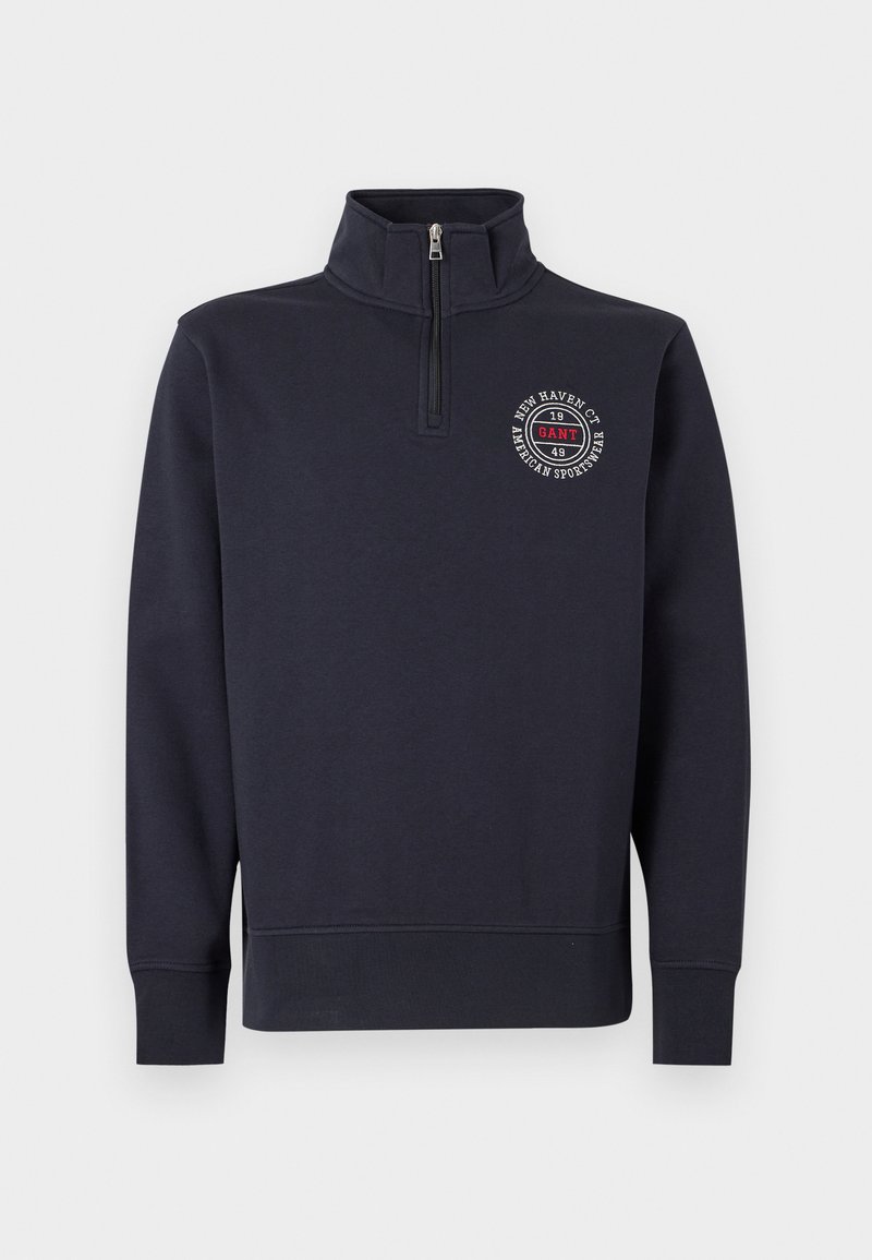 Pile blu navy con collo alto, chiusura con zip e logo sul petto frontale con design circolare e testo. Tessuto liscio, polsini a coste.