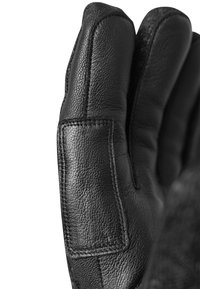 Der schwarze Lederhandschuh verfügt über ein strukturiertes Material mit markanter Naht. Die Hand ist teilweise geöffnet und zeigt die geschwungene Form und Details.