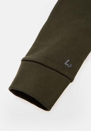 Mroczna oliwkowa zieleń rękaw bluzy z prążkowaną teksturą, z jasnoszarym logo w pobliżu mankietu. Gładki materiał z dopasowanym krojem.