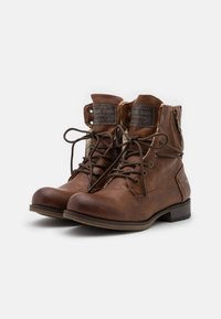 Brązowe skórzane botki za kostkę z sznurowadłami, zamkami błyskawicznymi z przodu i z boku, okrągłymi noskami, teksturowaną powierzchnią oraz logo Mustang Jeans na języku.