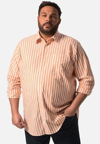 Una camicia a righe dai toni arancione chiaro e crema, con una tasca sul petto e maniche arrotolate, realizzata in un tessuto leggero e traspirante.