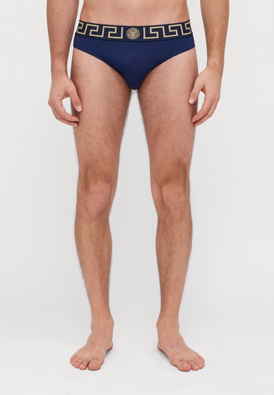 Marinefarbene Bikini-Slip aus glattem, dehnbarem Material mit einem goldenen griechischen Schlüssel-Muster am elastischen Bund und einem zentralen Logo.