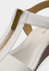 Λευκό δερμάτινο σανδάλι με χρυσό φερμουάρ στο λουράκι και επενδεδυμένο πέλμα, με καφέ τακούνι πλατφόρμας.