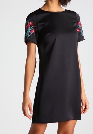 Black satin short-sleeve dress with red and green floral embroidery on sleeves, worn by a person shown from neck to mid-thigh.