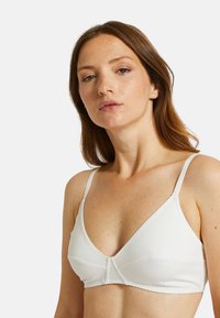 Bralette en coton blanc de forme triangle, avec des bretelles réglables et des détails de couture. Texture douce sans armature ni rembourrage.