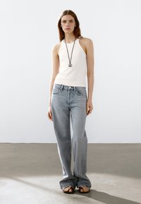 Blauwe denim jeans met een relaxed fit, gecombineerd met een witte geribbelde tanktop en een lange zwarte ketting. De jeans hebben een klassiek ontwerp met vijf zakken.