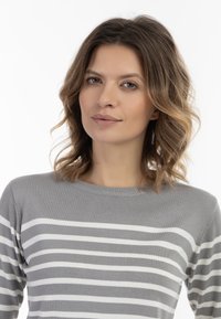 Maglione grigio a strisce con strisce orizzontali bianche, texture morbida, collo rotondo e vestibilità rilassata. Capelli naturali che incorniciano il viso.