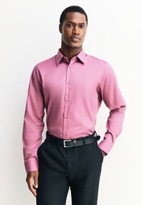 Różowa koszula wizytowa z długim rękawem, z ostrym kołnierzykiem, zapinana na guziki z przodu, wykonana z teksturowanej tkaniny, zestawiona z czarnymi spodniami i paskiem.
