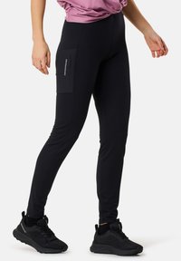 Black leggings with a fitted design, featuring a side pocket and subtle branding. Made from smooth, stretchy fabric, paired with black athletic shoes.