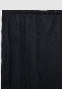 Tissu de dentelle noire présentant une surface douce et texturée avec des motifs floraux complexes, fini avec un bord supérieur élastiqué froncé.