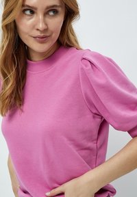 Rosa sweatshirt med korta puffärmar, ribbad rund halsringning och en mjuk, slät textur. Enkel design utan ytterligare mönster.