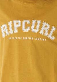 Musztardowa koszulka T-shirt z miękkiej tkaniny, z dużym, sfatygowanym białym napisem "RIPCURL" i napisem "AUTHENTIC SURFING COMPANY" znajdującym się poniżej.