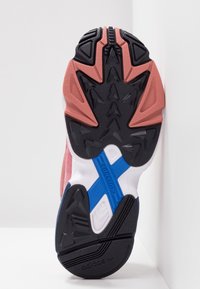 Soletta delle scarpe in gomma nera texturizzata, con accenti rosa, design blu e bianco a croce, caratterizzata da motivi di grip triangolari e supporto alla torsione.