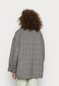 Veste surdimensionnée à motif pied-de-poule en gris et beige. Dotée d'un col pointu, d'un grand empiècement au dos et de manches avec poignets retroussés.