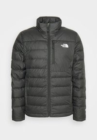 Veste noire matelassée et isolante North Face avec col montant, fermeture éclair devant, poche poitrine zippée et logo blanc sur la poitrine gauche.