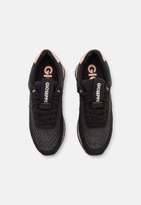 Sneakers neri con una tomaia in rete intrecciata, lacci neri a contrasto e dettagli rosa sulla linguetta, con una suola marrone texturizzata.