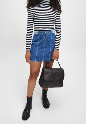 Femme portant un col roulé rayé noir et blanc, une jupe en denim bleu avec une fermeture éclair à l'avant, des bottes de combat noires, tenant un sac à main en cuir noir.