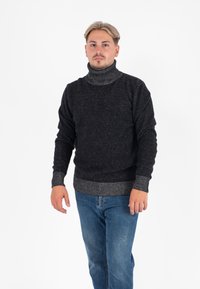 Sweter w kolorze węgla drzewnego z teksturowanym wzorem dzianiny oraz kontrastującymi ściągaczami przy kołnierzu i na brzegach; noszony z niebieskimi dżinsami.