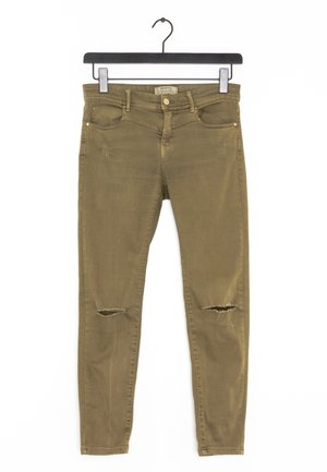 Olivgrüne Skinny-Jeans mit ausgefransten Rissen an den Knien, im Fünf-Taschen-Design und mit Reißverschlussschlitz, hängen an einem schwarzen Kleiderbügel.