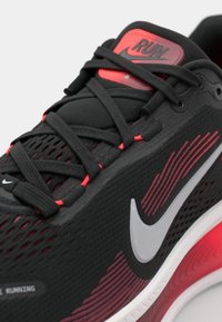 Baskets de sport noires et rouges avec tige en maille, logo Nike blanc et accents texturés. Comprend des lacets et un col rembourré pour le soutien.