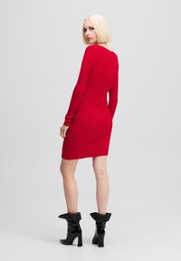 Rochie tricotată roșie cu nervuri, cu mâneci lungi și o formă ajustată. Pur și simplu cu botine negre din piele lacuită, cu guler evazat.
