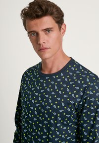 Lange mouwen marineblauwe shirt met een herhalend patroon van groene tennisrackets en ballen. Gemaakt van een zachte, lichte stof met een ronde hals.